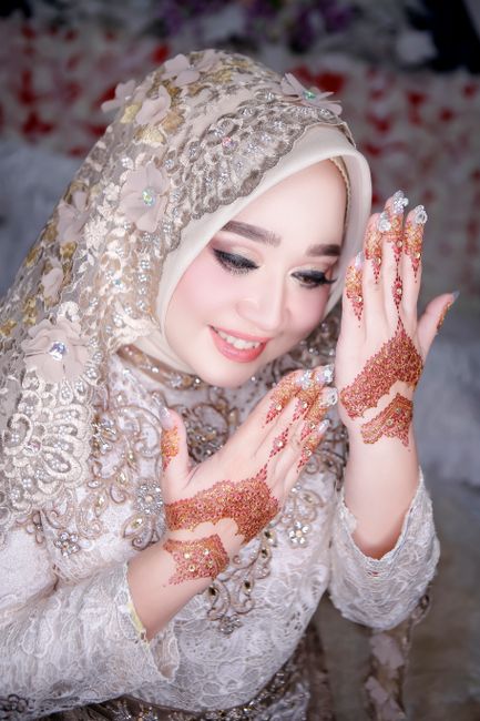 The image features a smiling bride wearing an ornate, cream-colored dress with intricate silver and gold embroidery, complemented by a matching hijab embellished with floral appliqués and delicate be