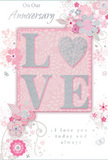 This anniversary card design is shown in close focus, blending soft pastel pinks and silvery greys into a scene of quiet, enduring romance that feels very at home in Downe's peaceful lanes. At the centre, the word LOVE is spelled out in raised, glittered lettering, each character smooth yet textured, with the O transformed into a shimmering heart picked out in silver for added emphasis. The glitter is fine and controlled, catching light like tiny flecks of frost on early-spring blossoms without appearing harsh or overly bright. Around this focal word, delicate blossoms in blush, mauve, and pale ivory unfurl in a style that suggests gentle watercolour, their edges softened as if slightly diffused by morning mist. Curving lines form stems and swirls, interspersed with tiny butterfly shapes and scattered petals that create a sense of movement, as though a light breeze is drifting through an English country garden near Downe's open fields. The floral motifs rest on a muted pink background, subtly shaded to add depth while remaining soothing and uncluttered. Across the top and lower portion, phrases such as On Our Anniversary and I love you today and always are rendered in a fine, flowing script, the lettering calm and sincere rather than overly ornate. The layout feels considered and balanced, much like an anniversary bouquet arranged by Flowers Downe for delivery to homes near High Elms Country Park-thoughtful, romantic, and designed to mark a shared journey with a soft yet profoundly heartfelt gesture.